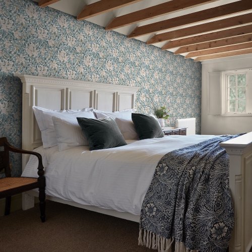 Room shot showing Honeysuckle Dusk Blue wallpaper with soft pink and gold highlights